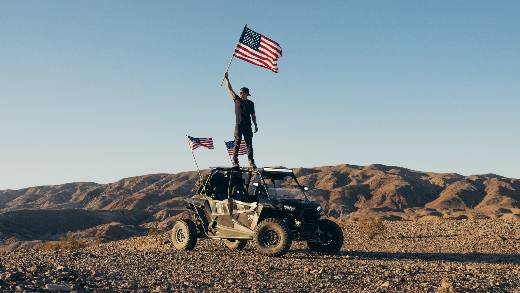 A man standing on Polaris RZR and waving flags
